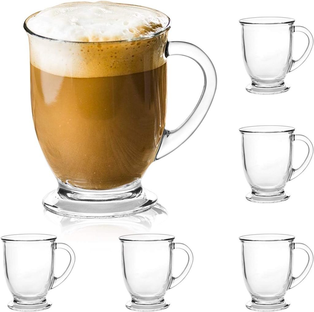 A glass mug filled with frothy coffee next to five empty glass mugs.