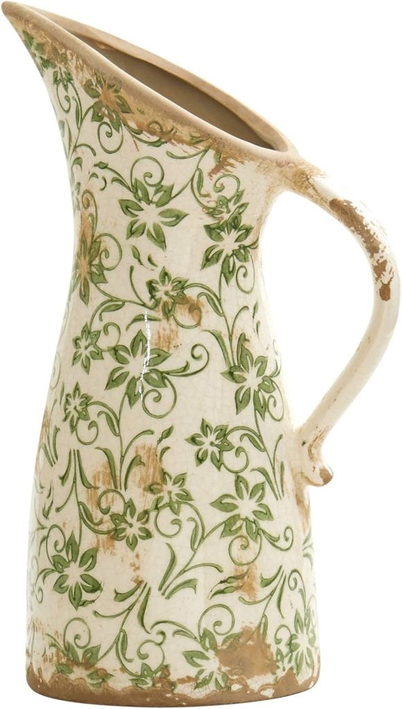 A vintage-style ceramic pitcher with a spout and handle, featuring a green floral design on a white background with distressed detailing.