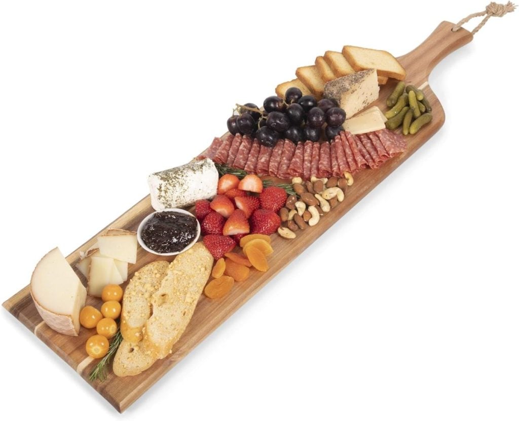 A delightful wooden board brimming with cheeses, meats, grapes, strawberries, nuts, pickles, dried apricots, and slices of bread makes the perfect centerpiece for any festive Christmas party.