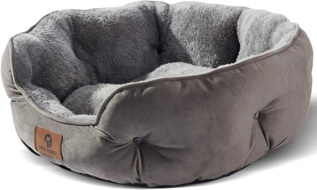 Round gray pet bed with a plush, soft interior and a faux suede exterior, featuring a stitched label on the side—perfect for pampering your furry friend during the season of giving.