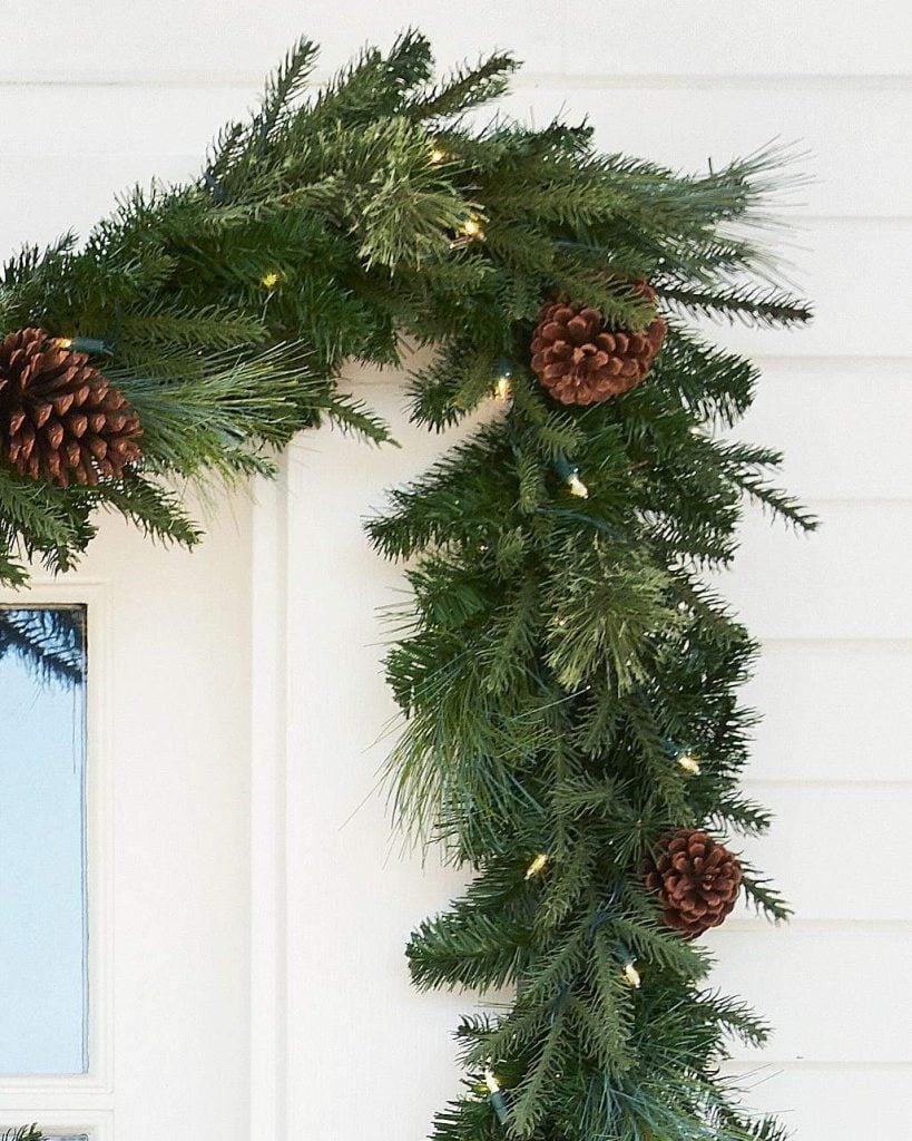 A green garland with pine cones and small lights decorates a white doorframe.