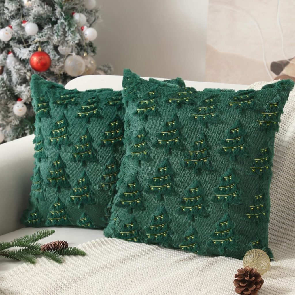 Two green Christmas pillows with festive tree patterns sit on a white couch next to a beautifully decorated Christmas tree.