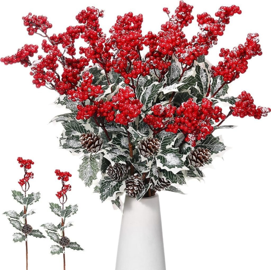 A vase holds red berry branches with frosted green leaves and pine cones.