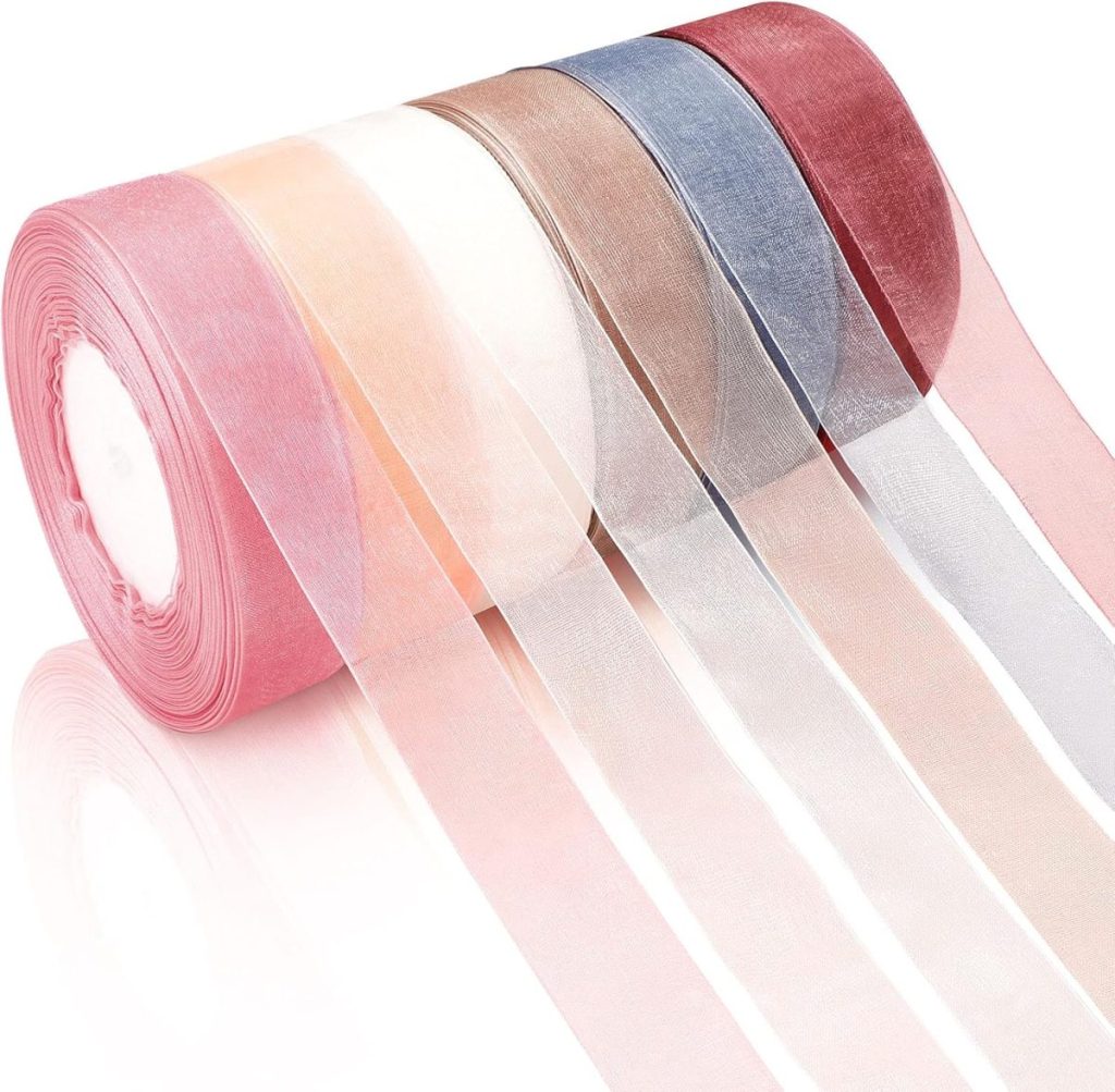 A roll of sheer organza ribbon in multiple colors—pink, peach, white, brown, blue, and red—unrolled and laid out, perfect for decorating gifts or pairing with glass Christmas ornaments.