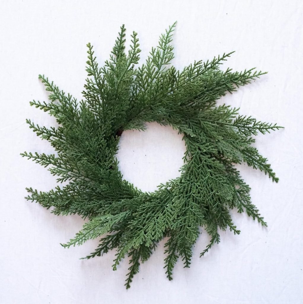 A simple green wreath made of evergreen branches arranged in a circular pattern on a plain white background.