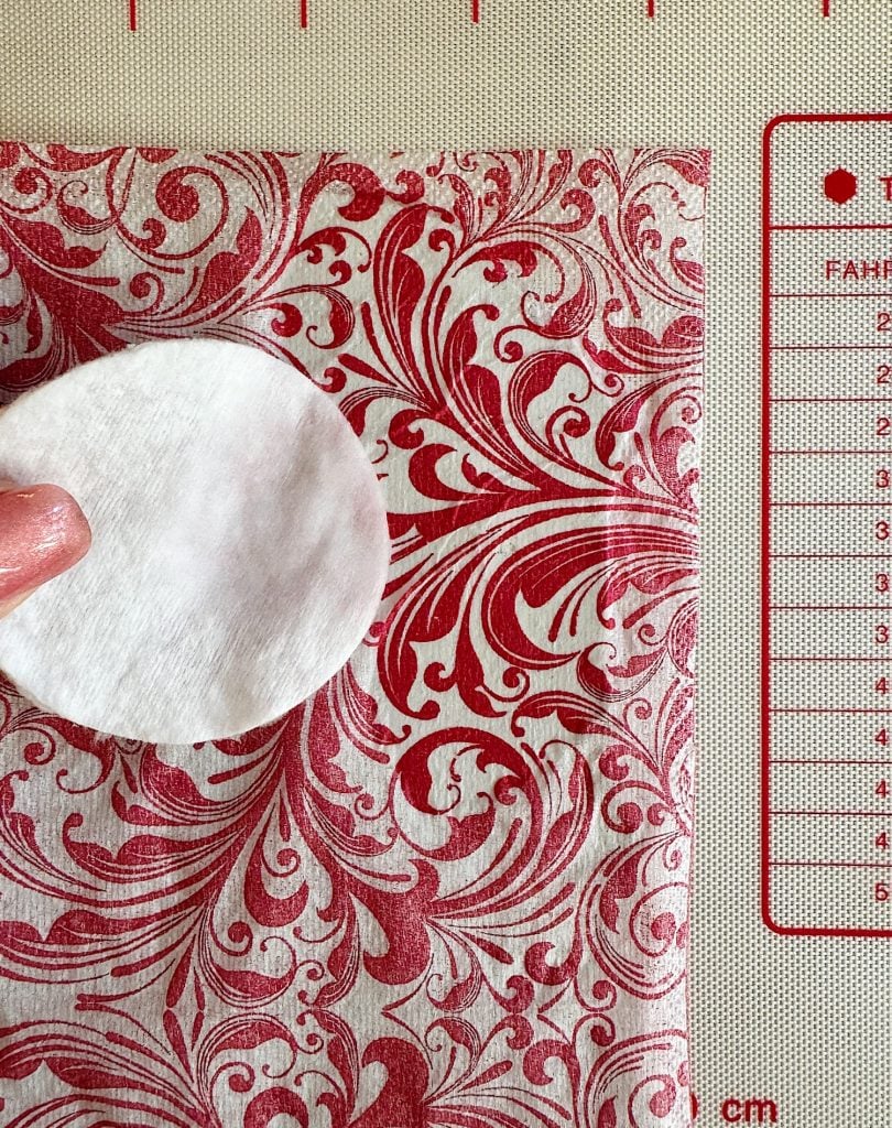 A white cotton pad is placed on red and white patterned fabric, next to a measuring guide with metric markings.