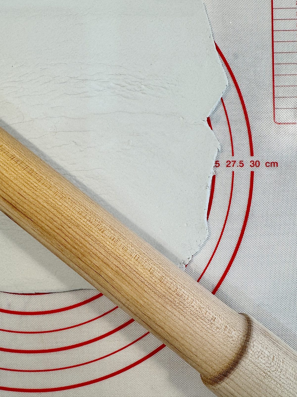 A wooden rolling pin on a red and white baking mat with rolled-out dough.