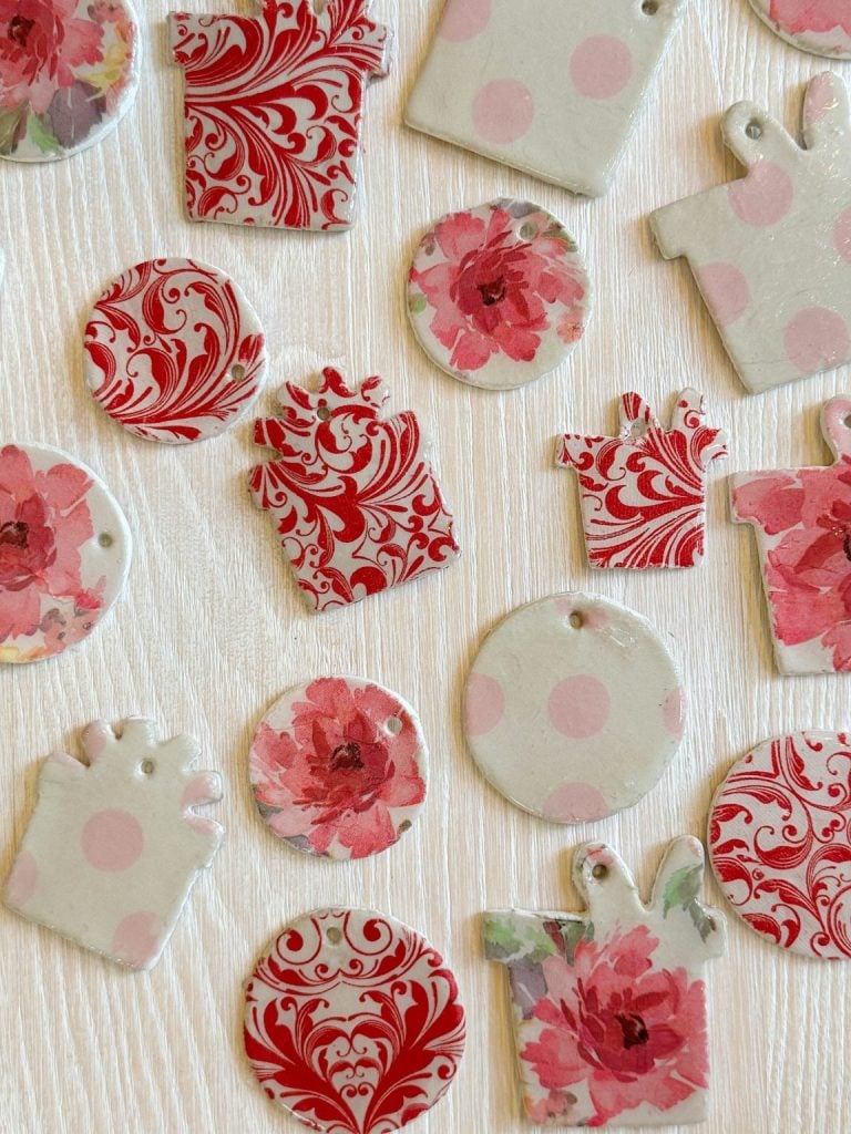 Red and pink floral and swirled patterned gift tag shapes on a light wooden surface.