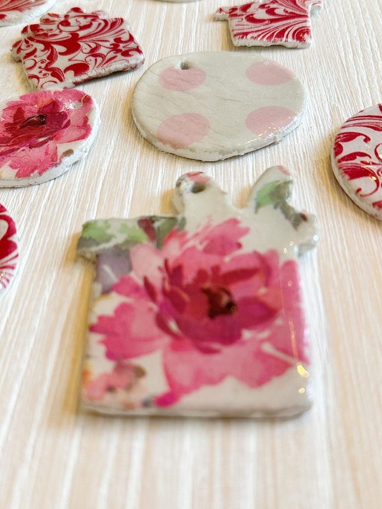 Close-up of various floral and patterned ceramic pendants on a light wooden surface.