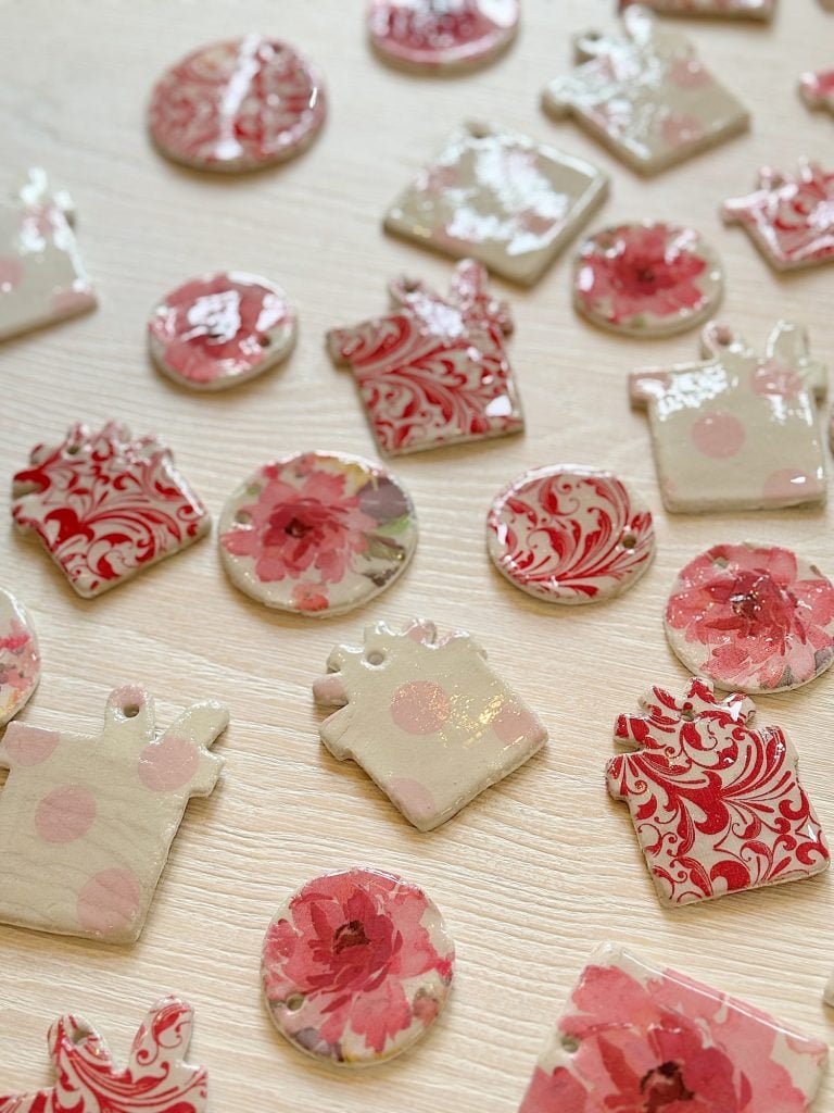 Handmade clay ornaments featuring pink floral and swirling patterns are scattered on a light wooden surface.