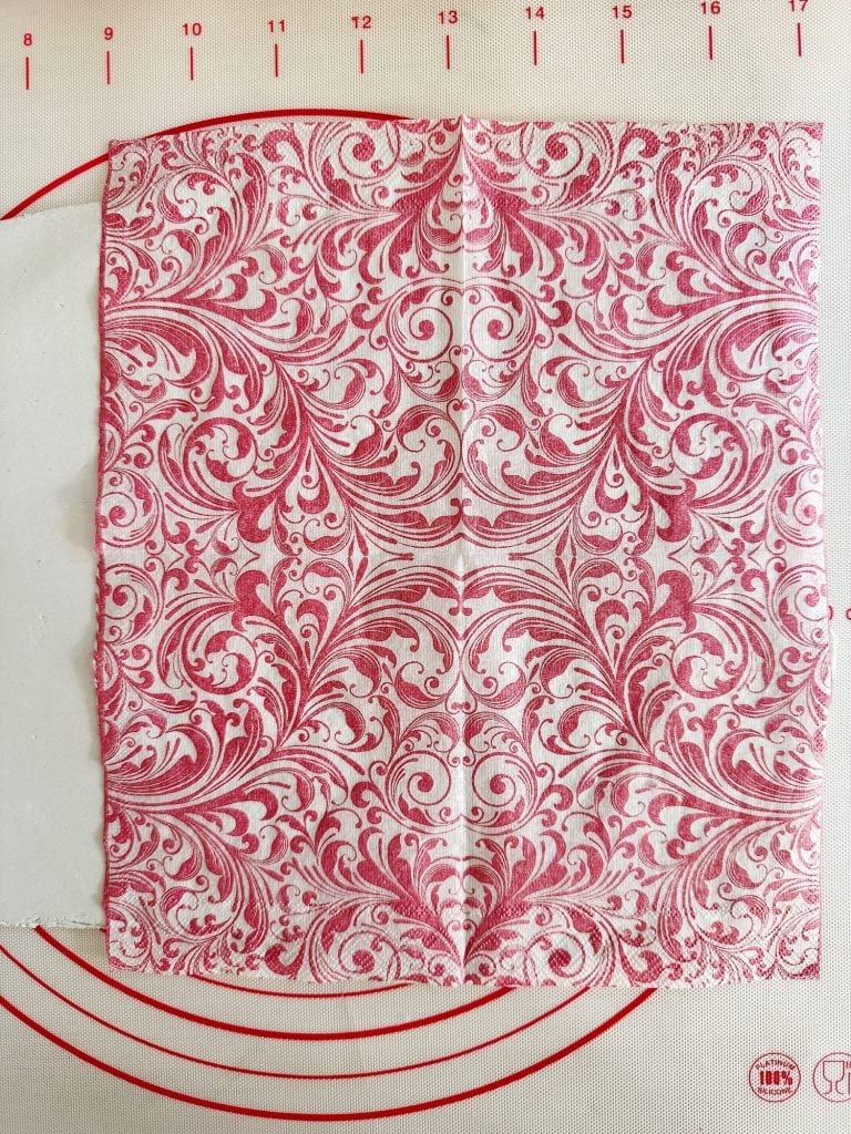 A square piece of paper with an intricate symmetrical pink and white floral pattern on a textured surface with red measurement markings.