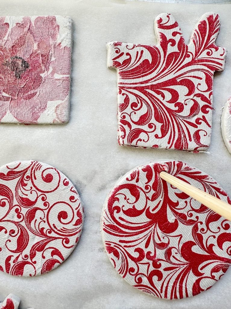 Craft pieces with red floral and swirl patterns on a white surface, including round and gift-shaped cutouts.