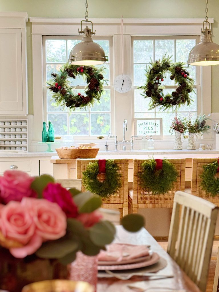 A kitchen decorated for the holidays with wreaths on windows and chairs, flowers on the table, and a sign that reads "Fresh Baked Pies Served Daily.