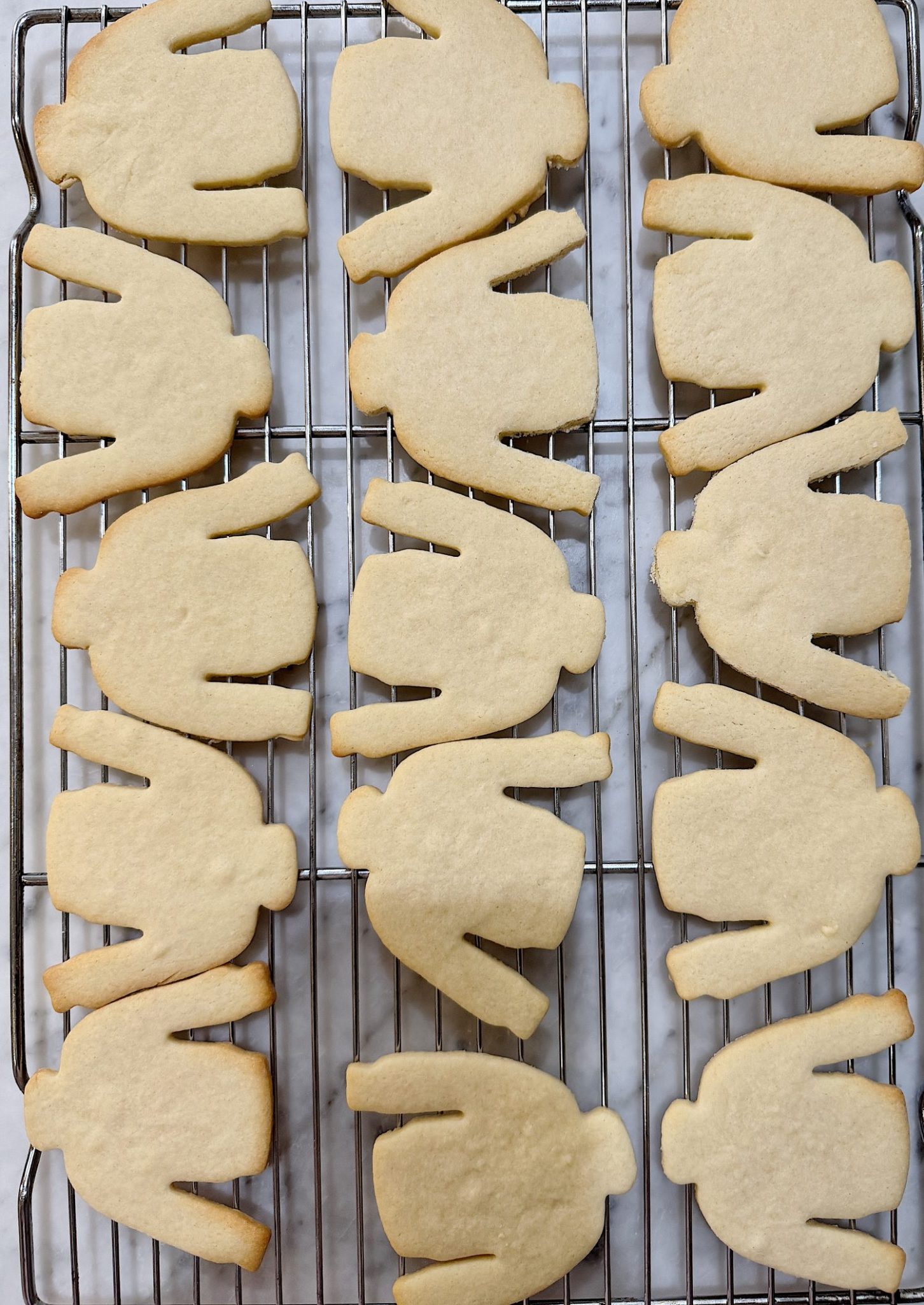 Twelve sweater-shaped sugar cookies cooling on a wire rack over a marble surface.