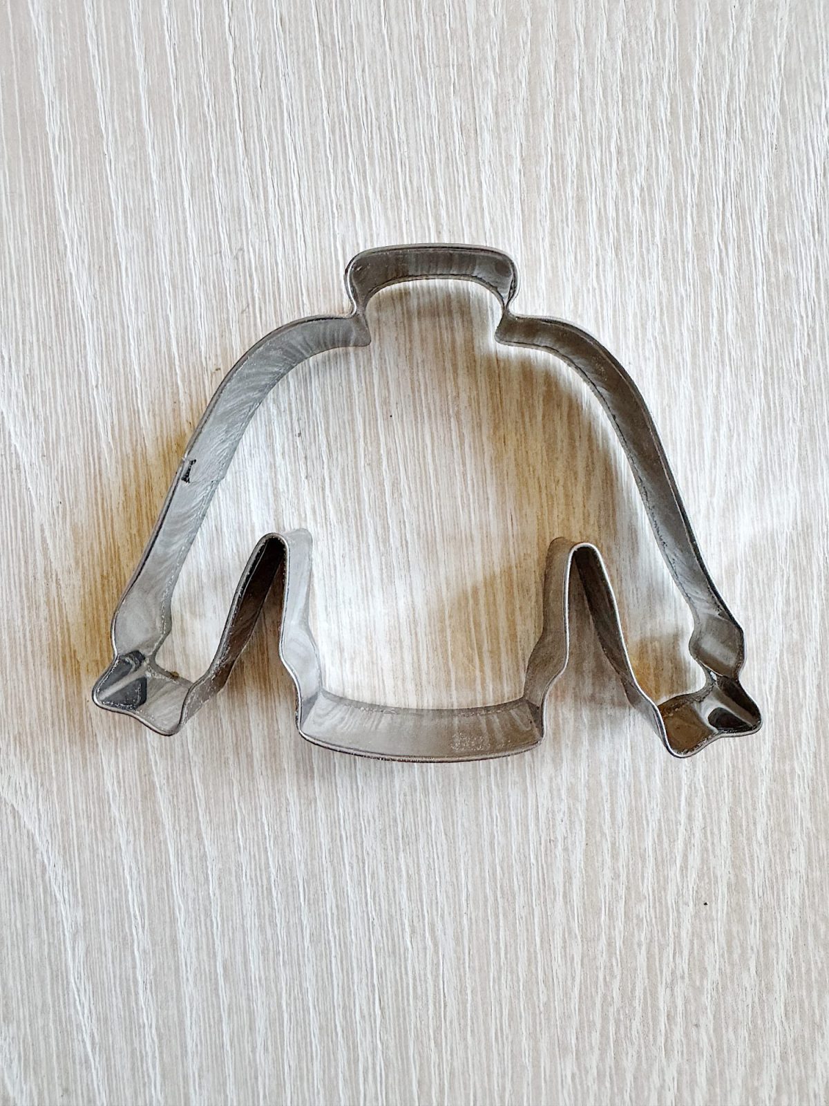 Metal cookie cutter shaped like a sweater on a light wooden surface.