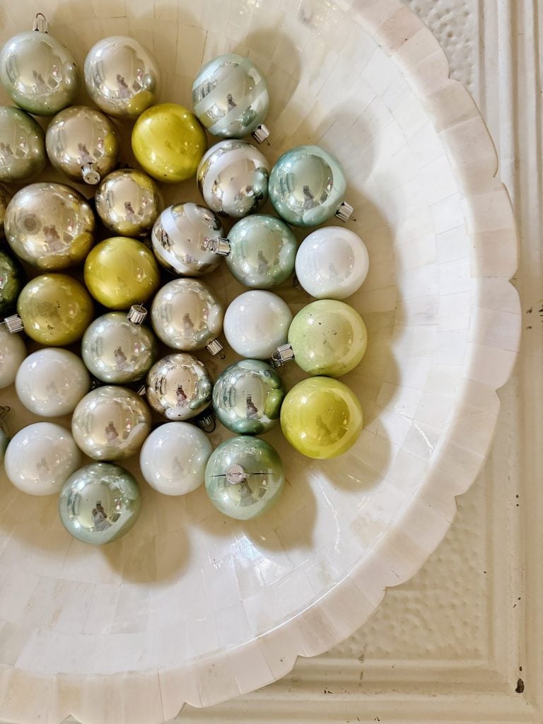 A bowl filled with metallic silver, green, and white Christmas ornaments.