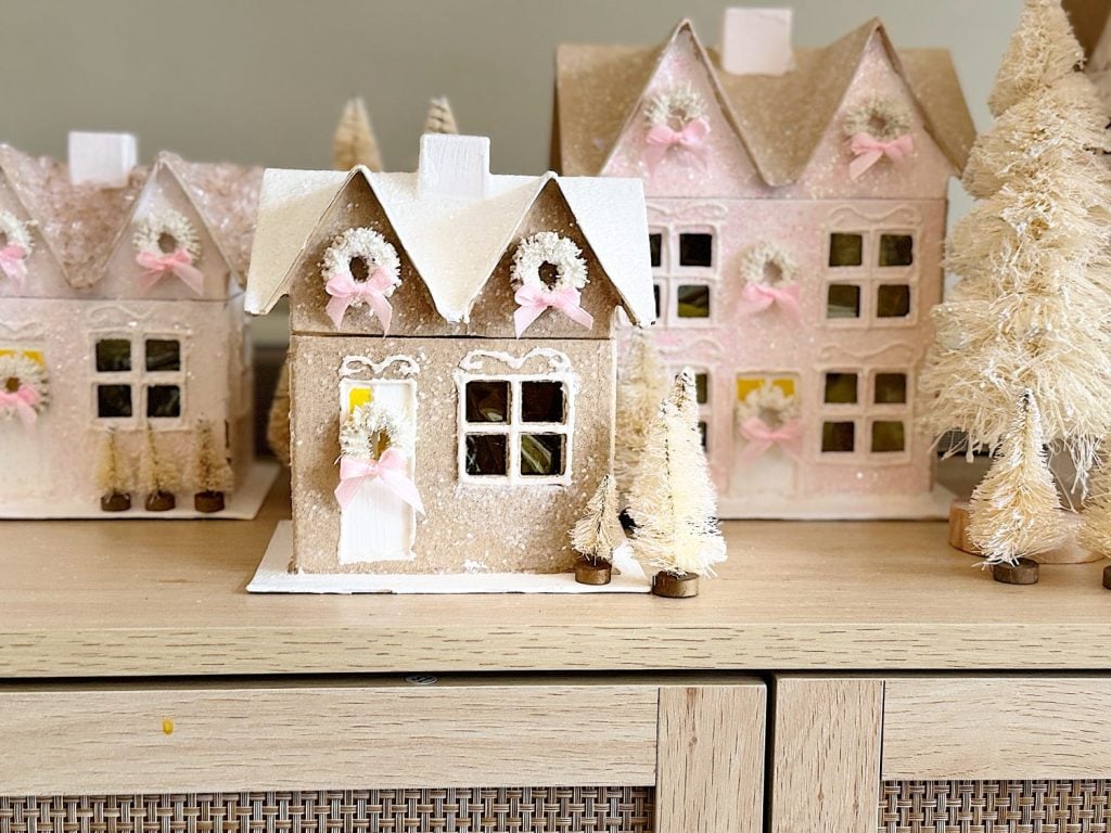 A collection of pastel pink and white decorative houses with festive wreaths and small artificial trees displayed on a wooden surface.