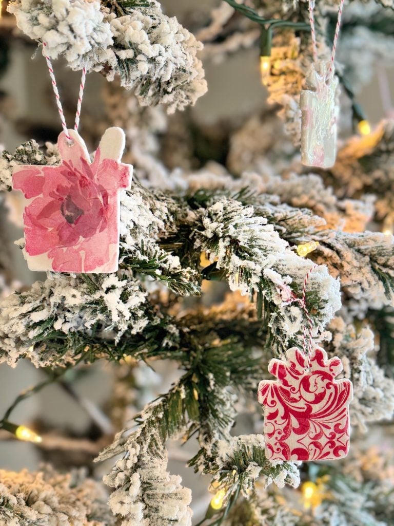 Close-up of a Christmas tree with snow-covered branches, adorned with pink and red patterned gift ornaments and warm fairy lights.