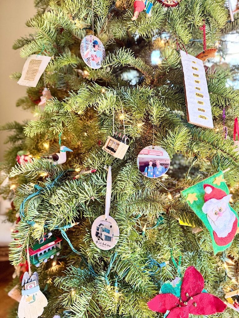 A Christmas tree decorated with various ornaments, including photos, a Santa cutout, a red flower, and a small train.