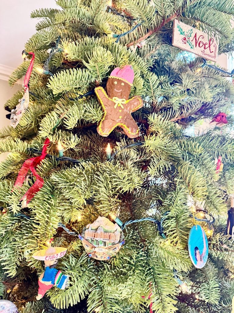 A Christmas tree decorated with a gingerbread man ornament, multiple baubles, and a "Noel" sign.