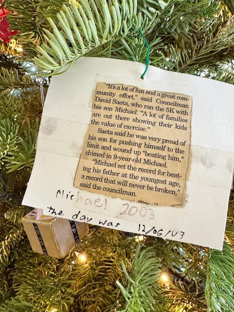 A newspaper clipping is attached to a Christmas tree with a tag labeled "Michael 2003 the day was 12/06/03" and a small wrapped gift hangs on the lower branch.