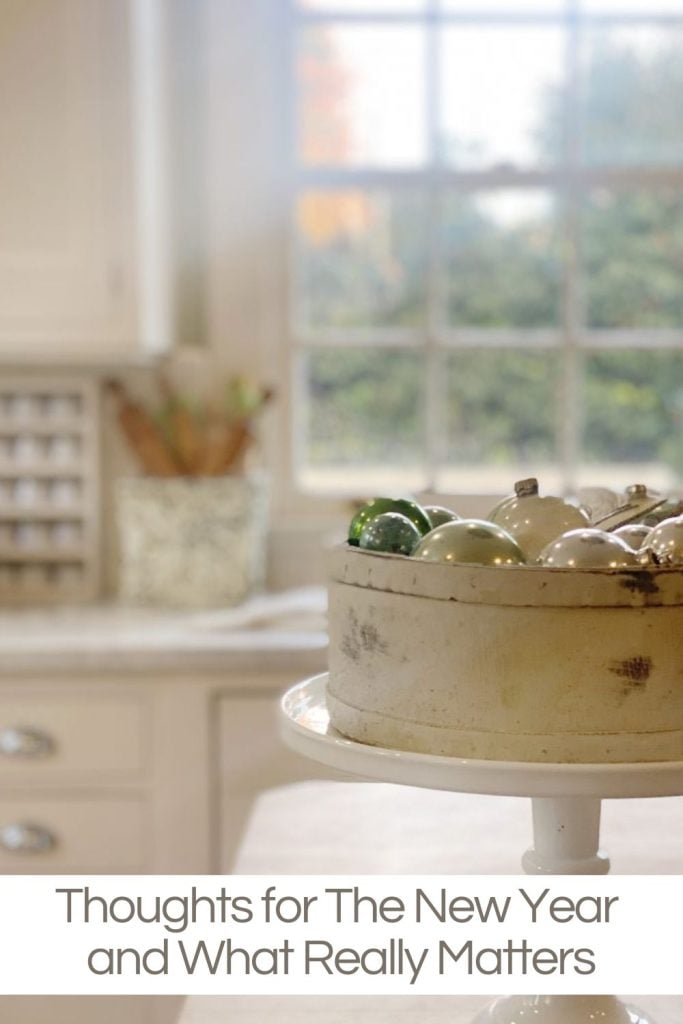 A kitchen with a window view, a cake stand holding ornaments on a counter, and a note reading "Thoughts for The New Year and What Really Matters.