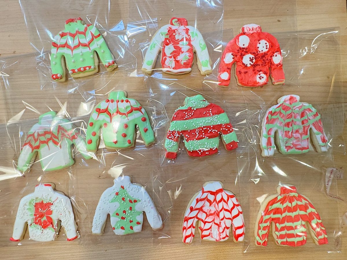 Twelve Christmas sweater cookies with colorful icing designs in red, green, and white on a wooden surface.