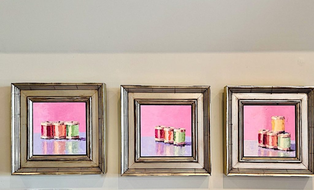 Three framed paintings featuring colorful sushi rolls on a pink background are displayed in a row on a light-colored wall, adding playful charm reminiscent of creative craft projects.