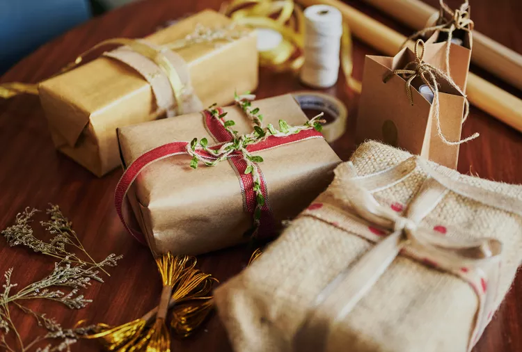 Assorted gift packages wrapped in brown paper and twine are placed on a wooden surface, decorated with various ribbons and dried plants.