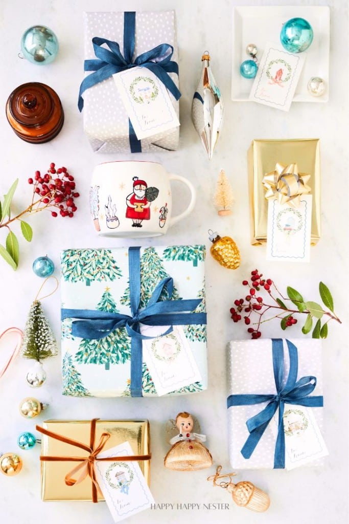 A flat lay of wrapped gifts with blue and gold paper, ribbon, and Christmas ornaments. Includes a Santa mug, small decorations, and festive tags.