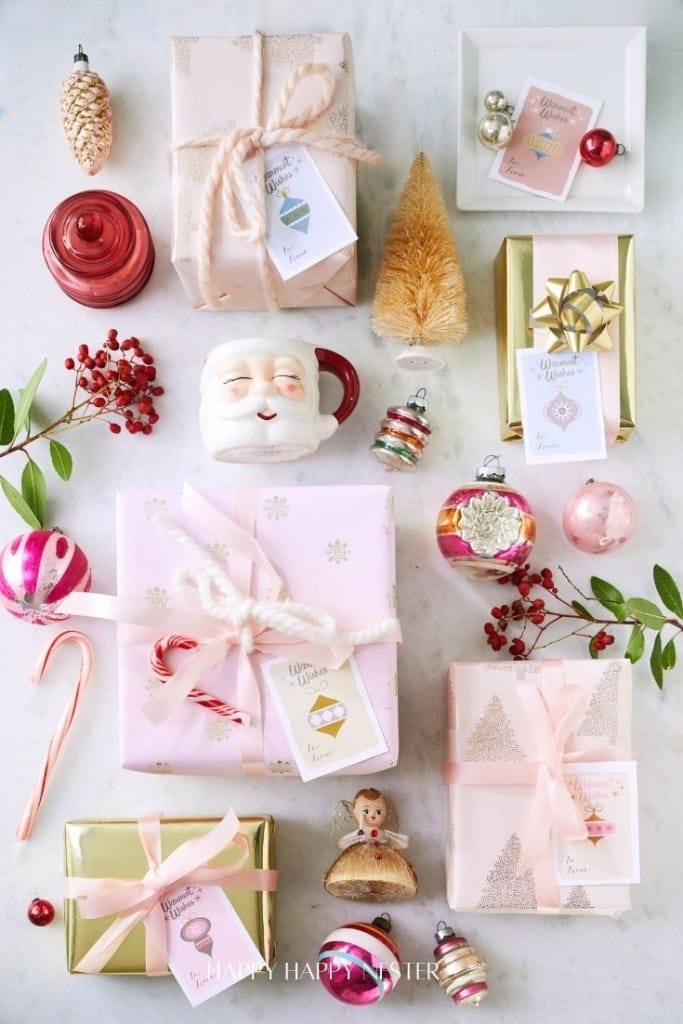 Assorted wrapped gifts and festive decorations, including ornaments, greenery, and a Santa mug, arranged on a light surface.