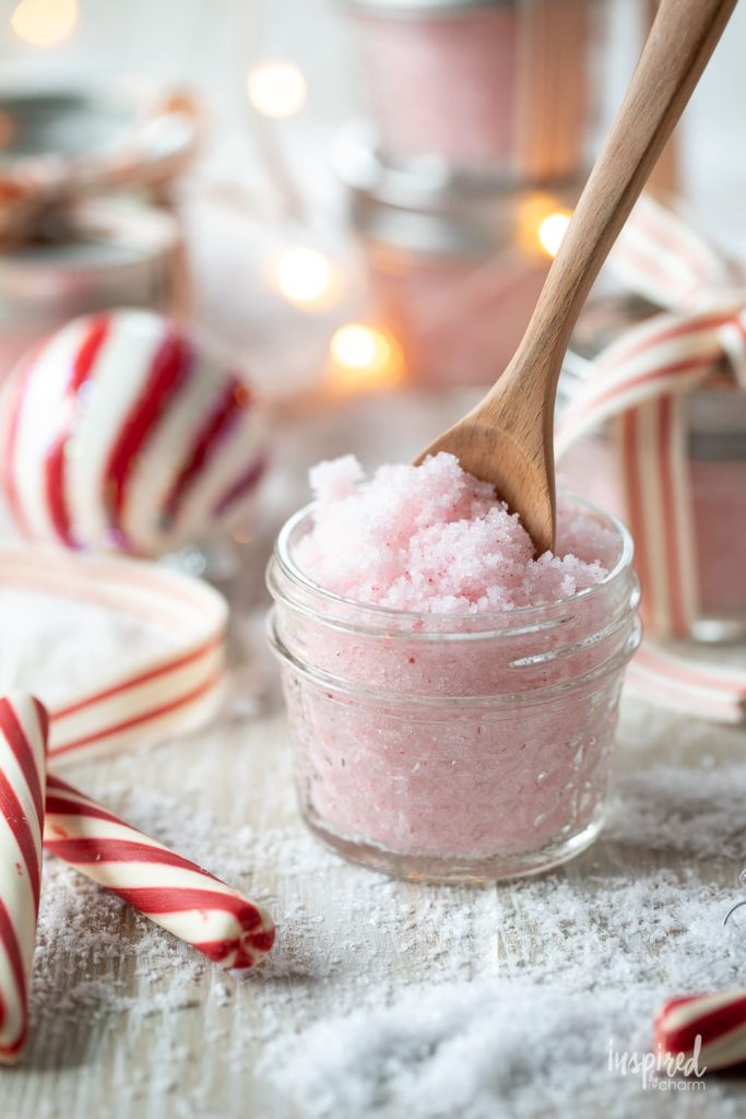 A jar of pink scrub with a wooden spoon, surrounded by candy canes and festive lights.