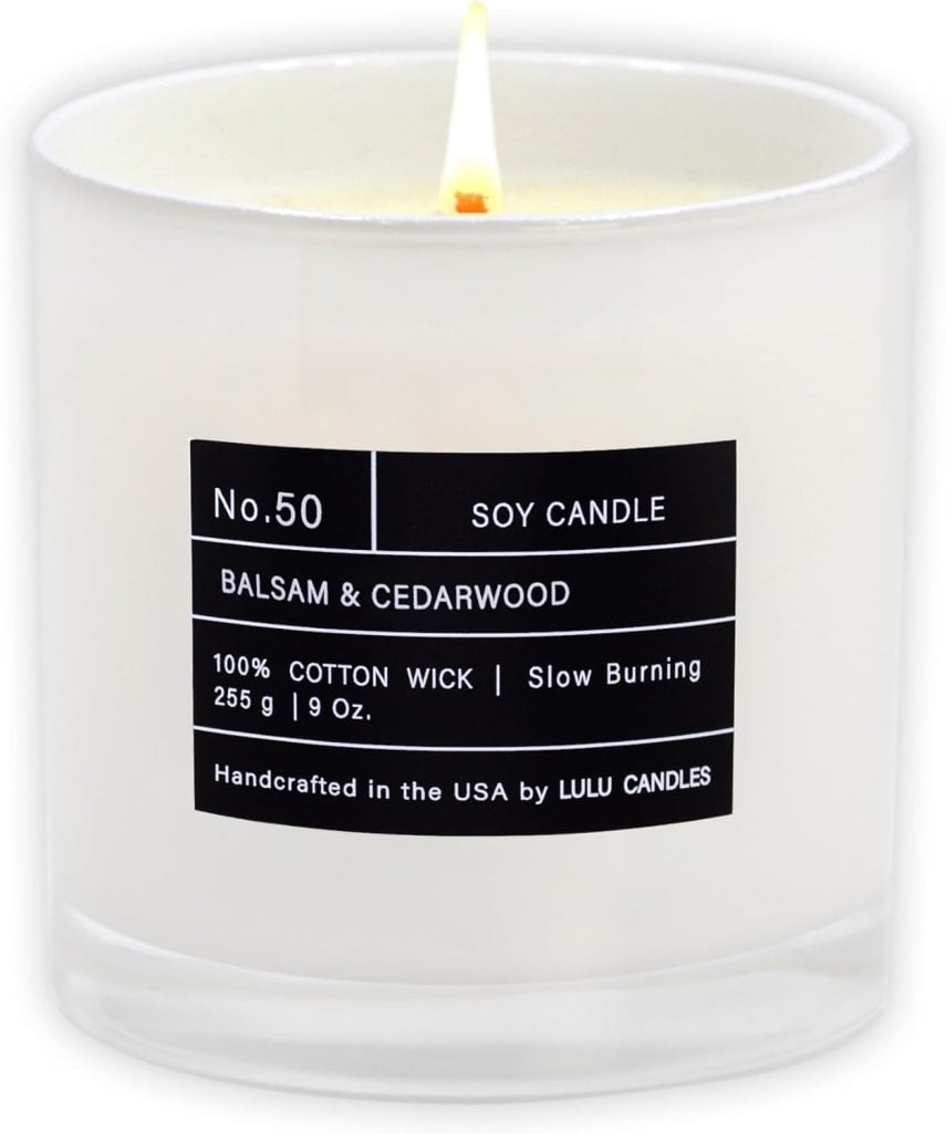 A lit soy candle labeled No. 50 balsam and cedarwood, with details about its cotton wick, slow burning, 255g weight, handcrafted by Lulu Candles in the USA.