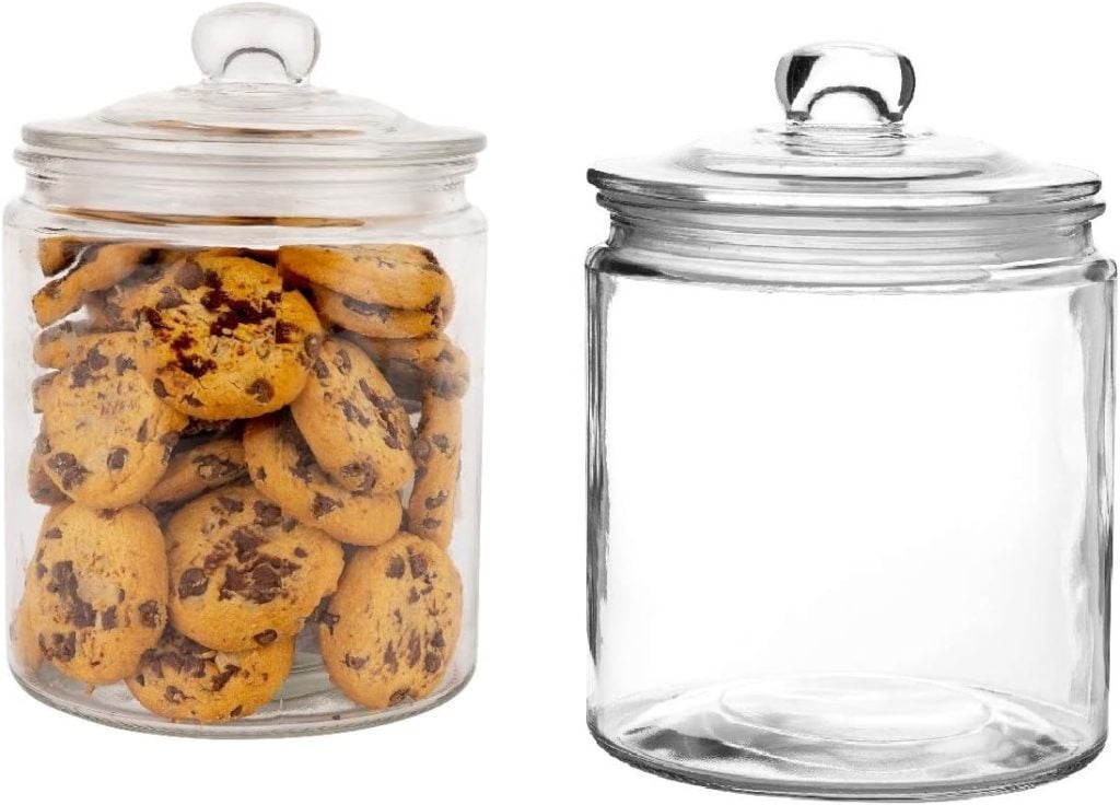 Two glass jars with lids sit on the counter; one is filled with chocolate chip cookies, while the other stands empty. These charming kitchen items add a touch of warmth and anticipation to any culinary space.