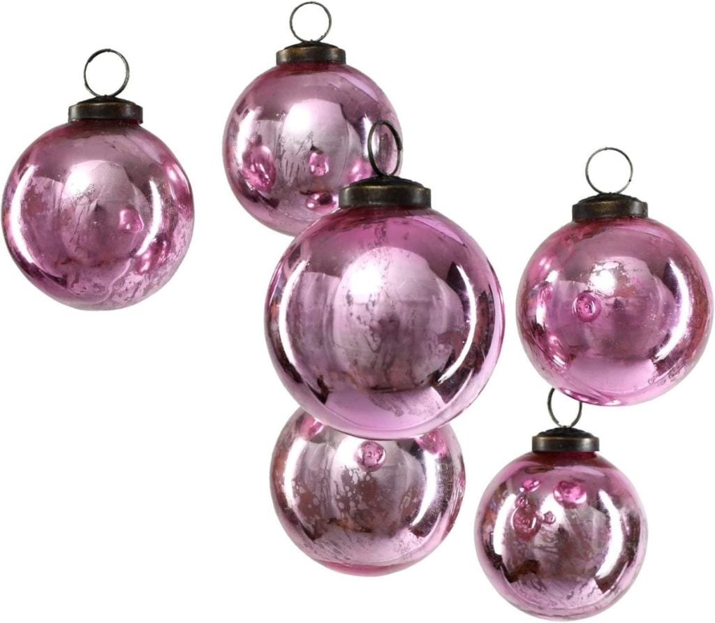 Six pink glass ornaments with metallic tops and loop hooks, reflecting light and showing some imperfections, arranged against a white background.