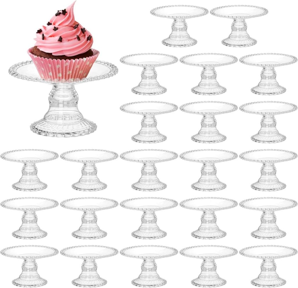 A single pink cupcake with star sprinkles sits on one glass pedestal stand, surrounded by empty identical stands arranged in rows&mdash;like a sweet centerpiece for a Valentine's Day Charcuterie Board.