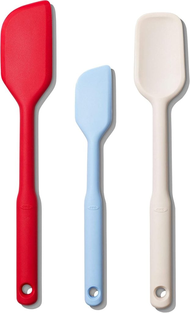 Three silicone spatulas in red, light blue, and off-white, essential kitchen items, are aligned vertically side by side.