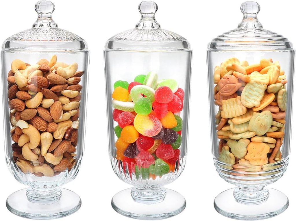 Three glass apothecary jars with lids contain assorted nuts, colorful gummy candies, and animal-shaped crackers, displayed side by side.