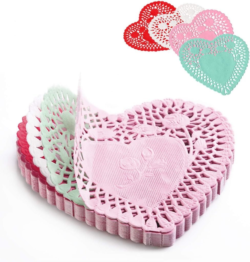 A stack of heart-shaped, lace-patterned paper doilies in pink, green, red, and white arranged in a pile, with one doily partially lifted.