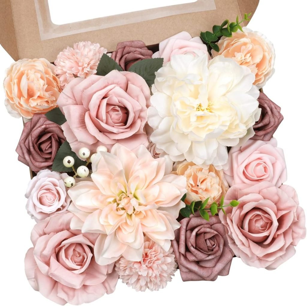 A box containing an assortment of artificial flowers, including roses and peonies, in shades of pink, cream, and mauve, with green leaves and small white berries.