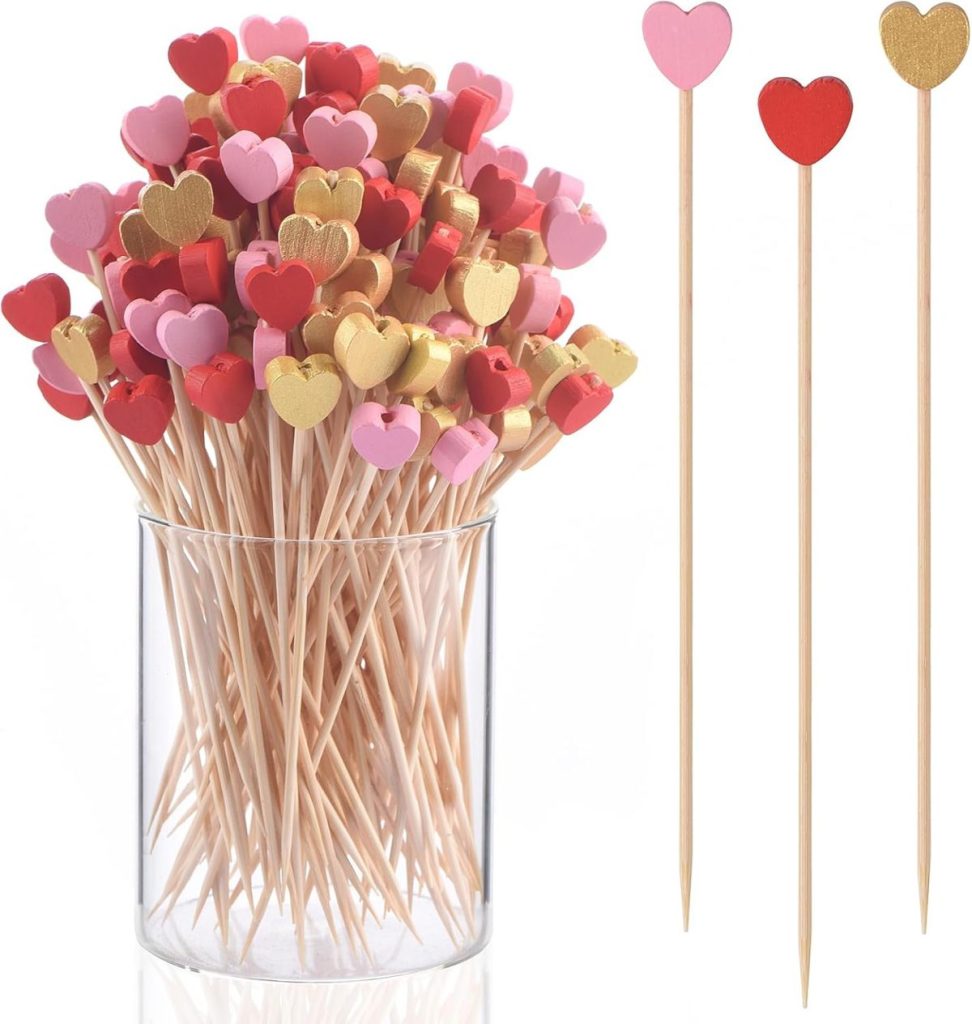 Wooden cocktail picks with red, pink, and gold heart-shaped tops in a clear container&mdash;perfect for serving chocolate marshmallow treats&mdash;with three individual picks shown separately on the right.