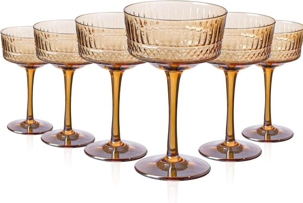 Six amber-colored vintage-style coupe glasses with patterned bowls and tall stems are arranged in two rows on a white background, perfect as chic Valentine table decorations.