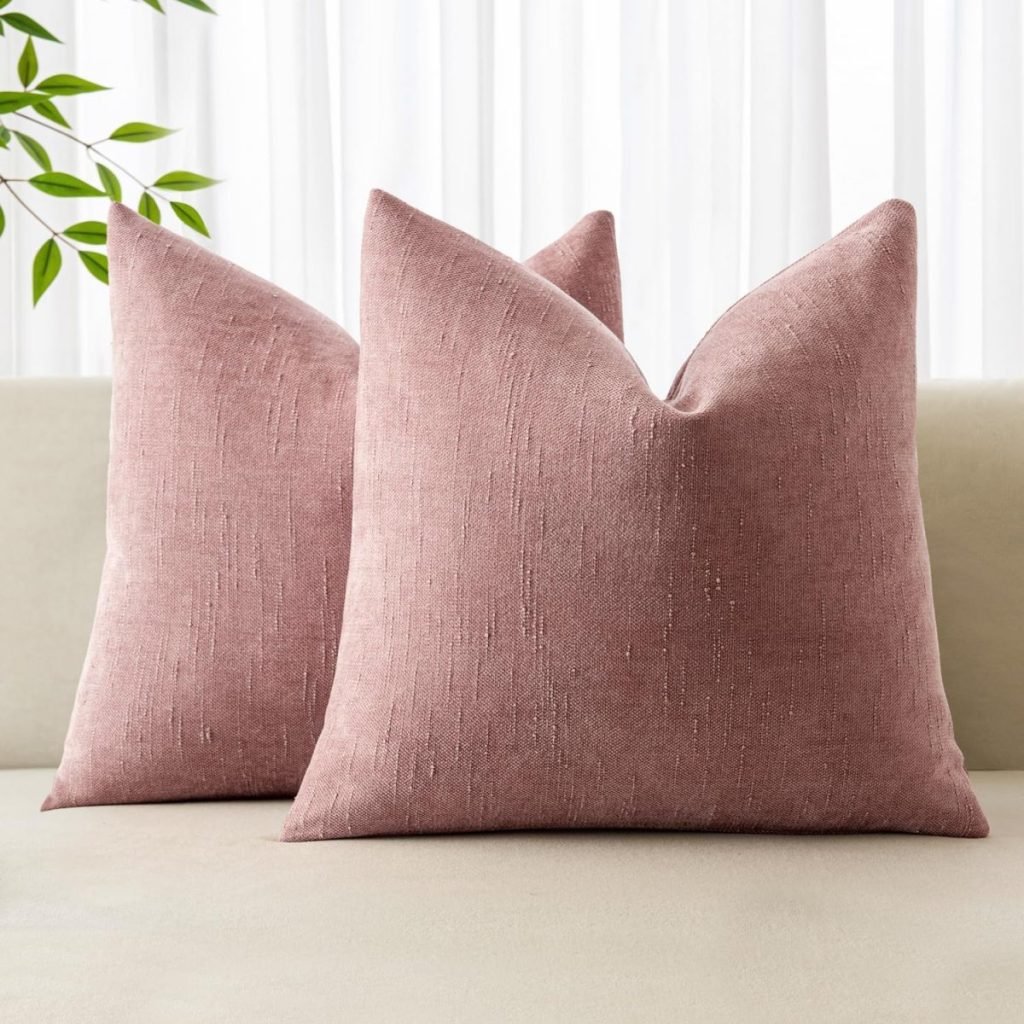 Two pink textured throw pillows on a beige couch, with a leafy plant in the background.