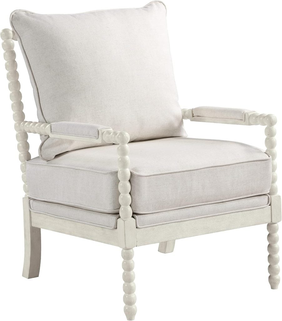 A white upholstered armchair with a cushioned seat and back, featuring decorative spindle-style wooden arms and legs, is accented by a charming heart pillow.