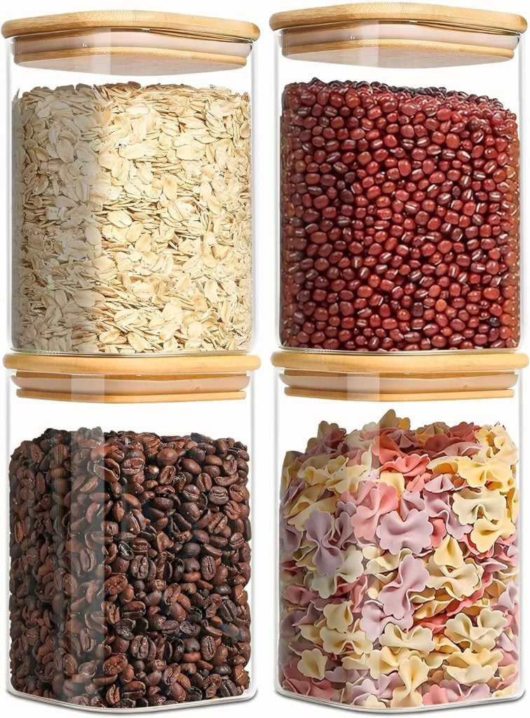 Four kitchen items, glass jars with bamboo lids, are beautifully filled with oats, red beans, coffee beans, and colorful pasta.