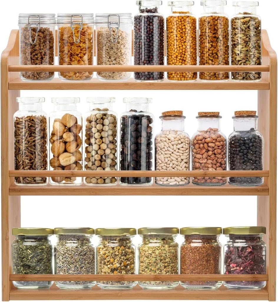 A wooden spice rack with three shelves showcases various kitchen items, including glass jars filled with spices and dried herbs, all arranged neatly in rows.