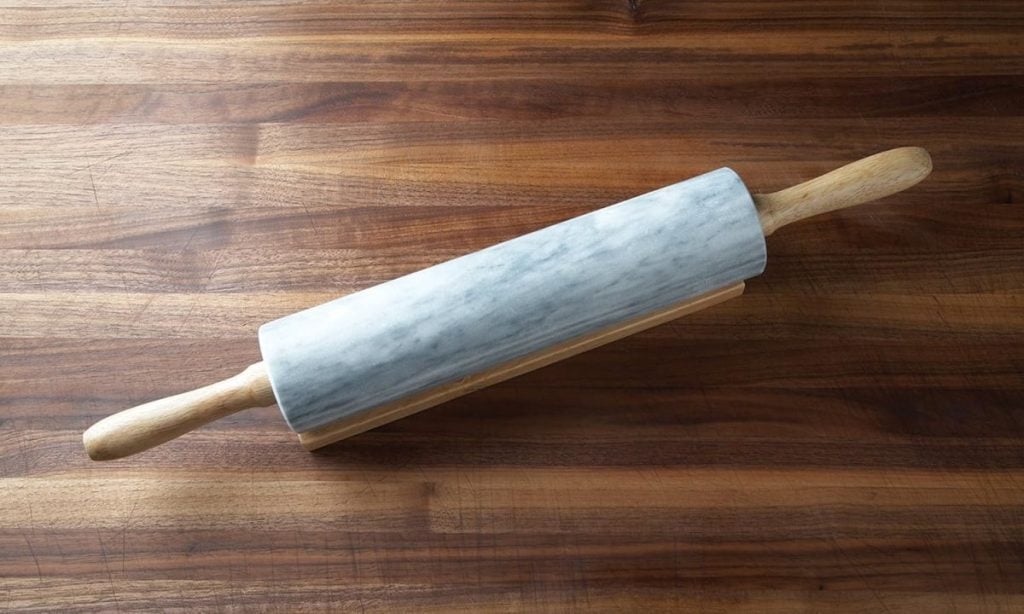 A marble rolling pin with wooden handles rests on a wooden surface.