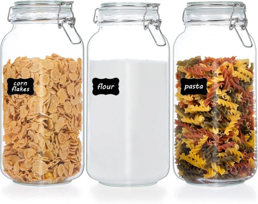 Three glass jars with locking lids showcase kitchen items: corn flakes, flour, and tri-colored pasta.