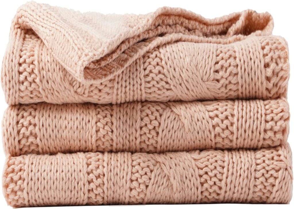 Three folded beige knitted blankets stacked on top of each other.