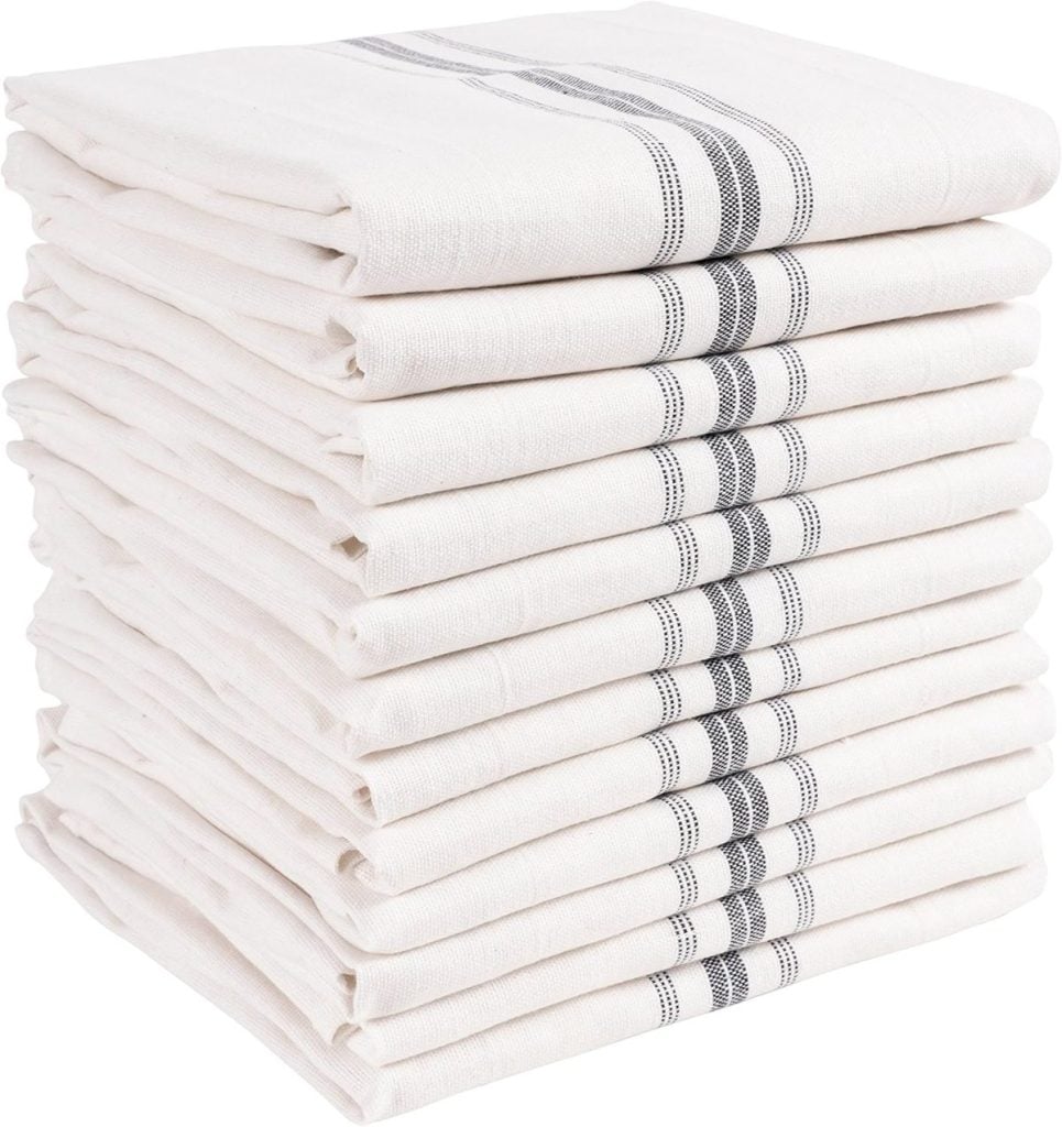 A stack of essential kitchen items, featuring white towels accented with three bold black stripes, is neatly arranged.